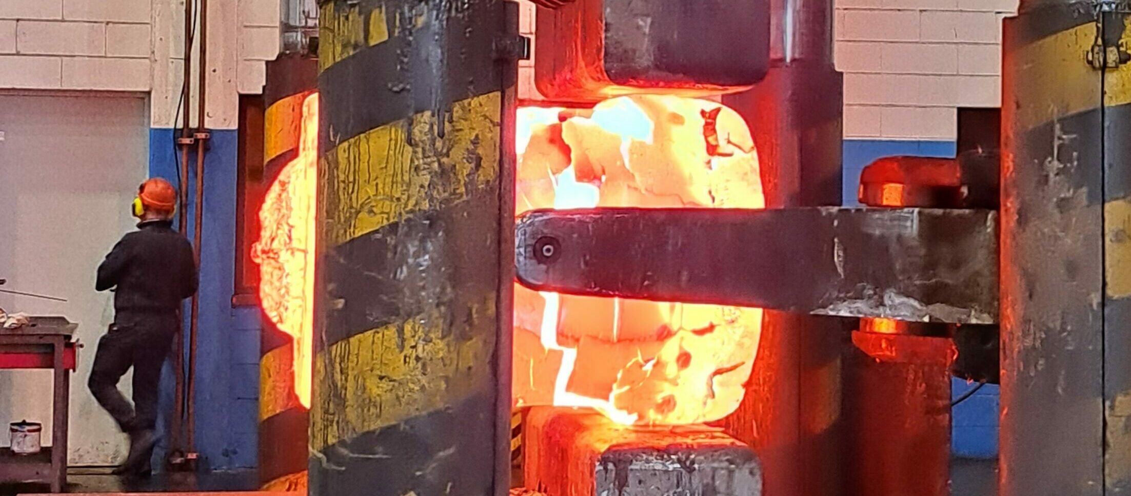 A glowing hot steel ingot being forged under the press